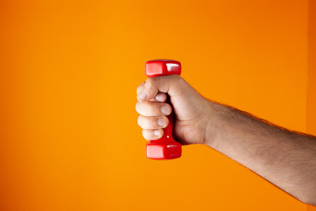 man holding small dumbbells on orange background
