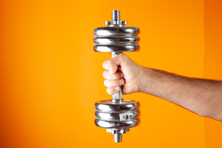 man holding dumbbell on orange backgroundの写真素材