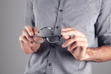 young guy holding optical glasses on gray  backgroundの写真素材