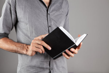 man reading a book while standing on gray backgroundの写真素材