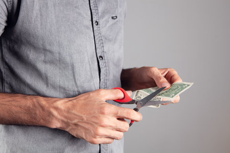 man cuts a dollar bill with scissorsの写真素材