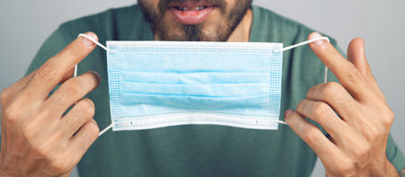 man holding a medical mask in his hand on a gray background