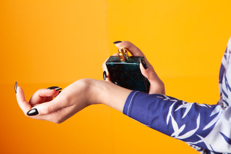 woman sprinkles perfume on her hand on an orange backgroundの写真素材