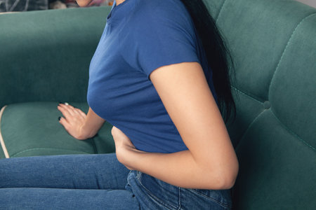woman sitting on the couch holds her stomach in painの写真素材