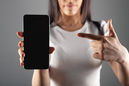 young woman shows phone on gray backgroundの写真素材