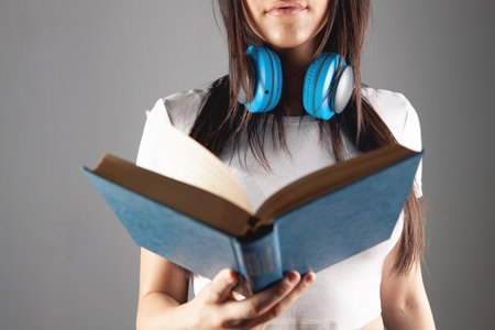 a young girl stands in headphones with a book