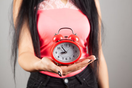 young woman holding an alarm clock on gray backgroundの写真素材