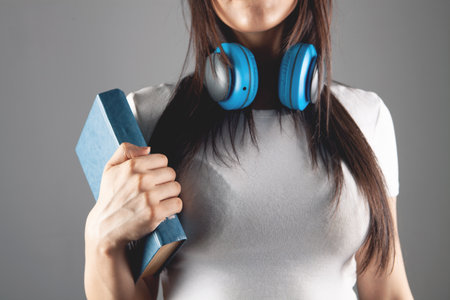 a young girl stands in headphones with a bookの写真素材