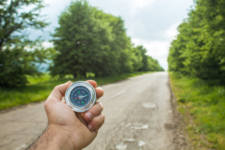 holds a compass on the background of the road and trees