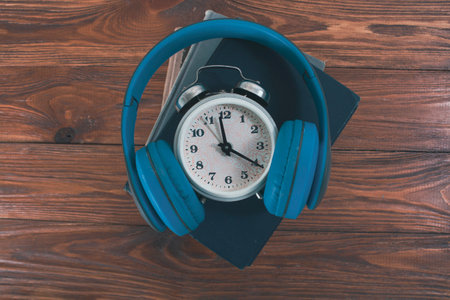 alarm clock, headphones and books on a wooden table. concept time for audiobookの写真素材