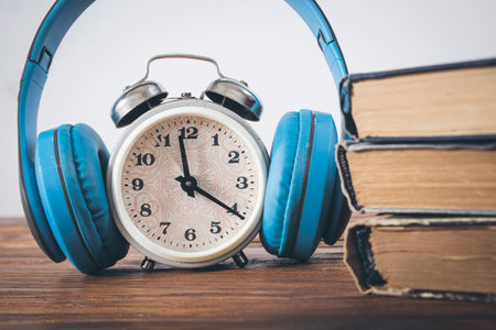 alarm clock, headphones and books on a wooden table. concept time for audiobookの写真素材