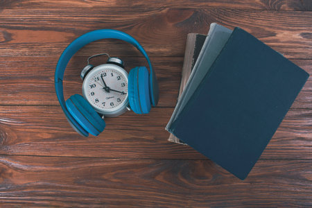 alarm clock, headphones and books on a wooden table. concept time for audiobookの写真素材
