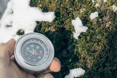 holding a compass on a background of moss covered with snow