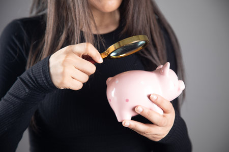 woman looking at a piggy bank with a magnifying glassの写真素材