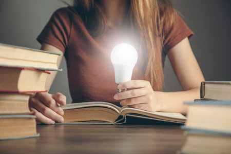 woman holding a light bulb while sitting in front of books. concept idea from the book