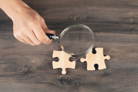 a woman with a magnifying glass looks at a puzzle pieceの写真素材