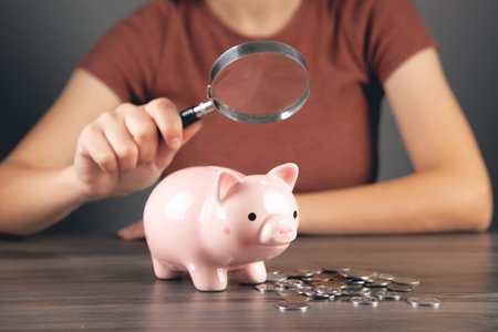 woman with a magnifying glass looks at a piggy bank and coinsの写真素材