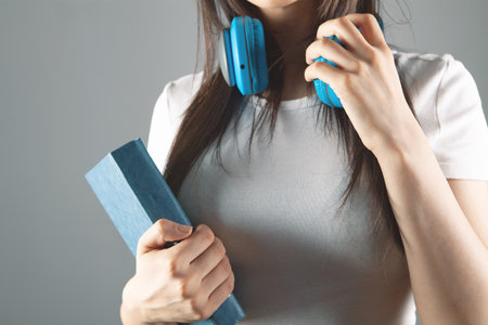 a young girl stands in headphones with a bookの写真素材
