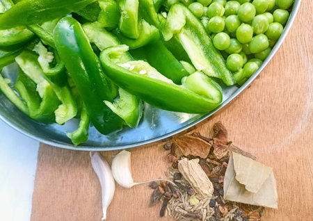Bell peppers and peas in a Metal plate with garlic and hot spices on a wooden table.