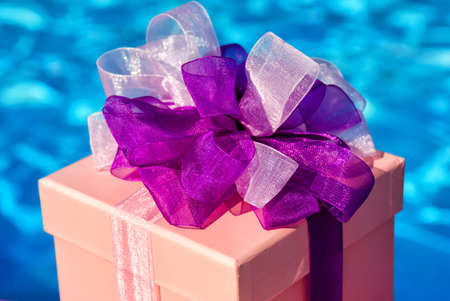 Gift box on the background of a blue pool. Craft from ribbons and colored paper, decorated with satin ribbon bows. Happy Holidays.の写真素材