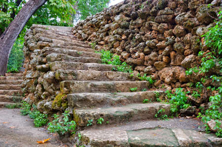 Ancient stone path stairs made of wild stone in a hilly park. Moss- and grass-covered stairs in the...