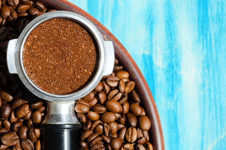 Coffee cone and ground coffee lie on coffee beans and on a ceramic plate. On a turquoise background.