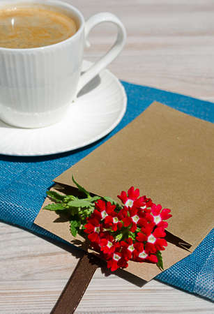 A cup of coffee and a saucer on a white table. Nearby is a romantic envelope with a flower and a turquoise scarf.の写真素材