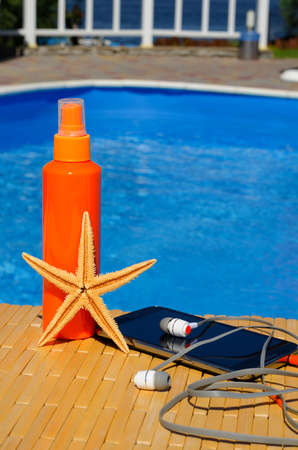 Starfish, sunblock, mobile phone and headphones on the background of a blue pool. On a summer sunny day.の写真素材