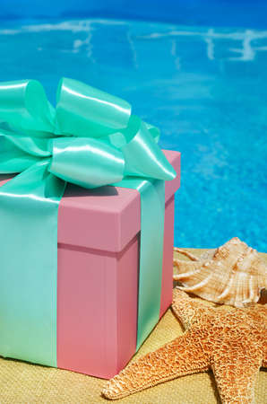 Gift box and a large starfish on the background of the pool. The pink box is decorated with a green ribbon on a background of turquoise water.の写真素材