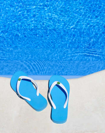 Slippers are on the edge of the pool. Bright blue flip-flops on the background of the pool.の写真素材