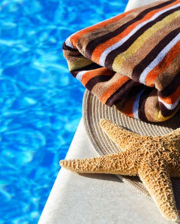 A big starfish and a colorful towel next to the pool. Multicolored bath towel against blue water background.の写真素材