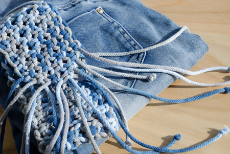 Macrame bag for mobile phone. Handmade clutch and jeans on the table. Hobby, needlework, knots.