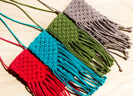 Small bags knitted with macrame technique. Multicolored mobile phone bags on a wooden background.