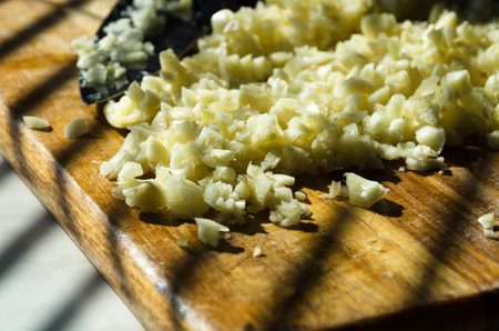 Chopped garlic on a wooden cutting board in a home kitchen. Chopped garlic in the rays of sunlight.の写真素材