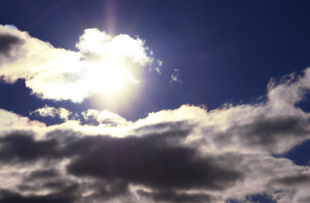 Bright light of the sun on a dark blue sky among the clouds. Dramatic view of the sun.の写真素材