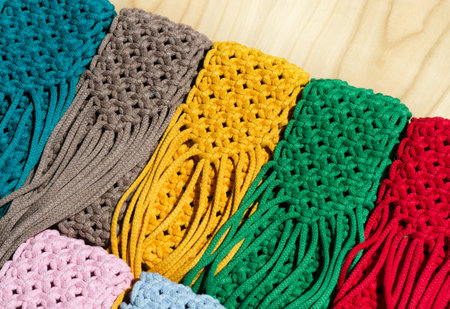 Small bags knitted with macrame technique. Multicolored mobile phone bags on a wooden background.