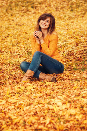 autumn fashion portrait of a positive woman in the casual style sitting on a yellow fallen foliageの写真素材