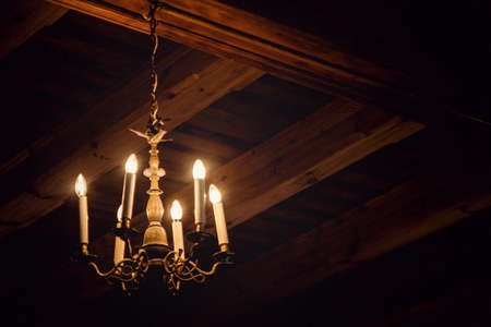 Dimly burning antique chandelier in an attic with wooden beamsの写真素材