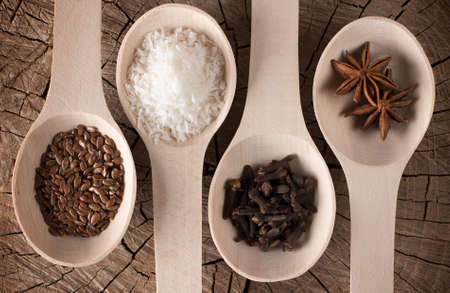 photo of lying deep kitchen spoons with kinds of condiments for drinks and sweet presented as grated coconut, cloves, star anise, seeds of flaxの写真素材