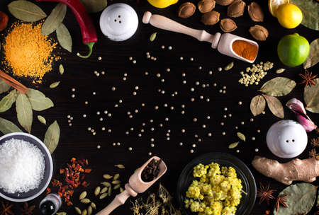 photo frame on top of herbs and spices for cooking lying on a wooden kitchen table: Hypericum, turmeric, bay leaves, coconut, lime, lemon, cinnamon, star anise, fenzel, garlic, ginger, with a place for write your ad textの写真素材