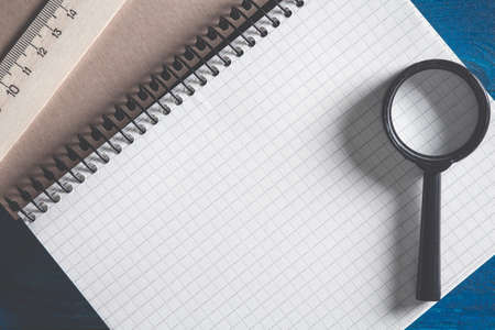 Photo of thick notebook to spiral into the cell lying on the table with a magnifying glass and a...