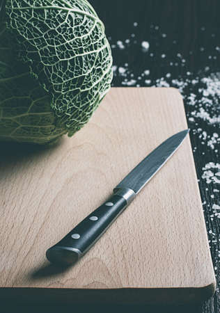 Savoy cabbage and knife on a cutting board on a black table with saltの写真素材