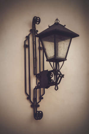 Old dirty street lamp hanging on the wall of the house made in an old style of metal with curlsの写真素材