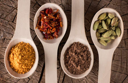background of deep wooden spoons lying in a row on a kitchen table with spices for food: dried red pepper slices, turmeric, cinnamon, fennel seedsの写真素材