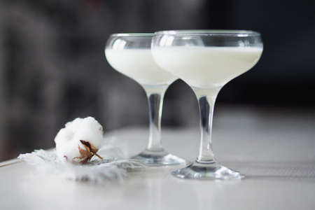 Two glasses filled with milk and put together with a cotton flower and thuja