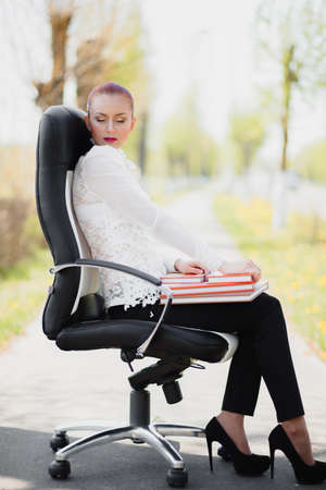 Beautiful girl sitting on the leather office chair with book outdoorの写真素材