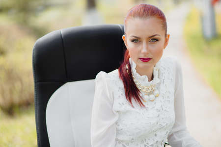 Beautiful girl sitting on the leather office chair outdoorの写真素材