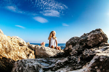 Beautiful girl with perfect hair sitting on rocky seashore with the bouquet of seashellsの写真素材