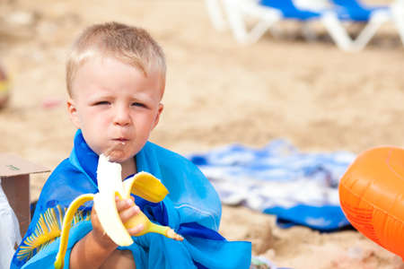 Small beautiful boy with banana on the sand in summerの写真素材