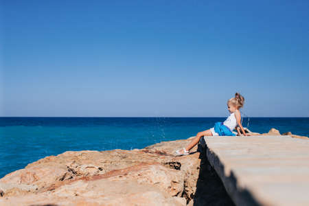 Beautiful girl posing on the rocky seashore sitting on the bridge